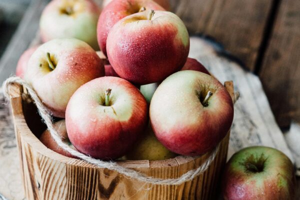 A close-up of ripe apples in a wooden basket on rustic planks. Ideal for fall harvest themes.