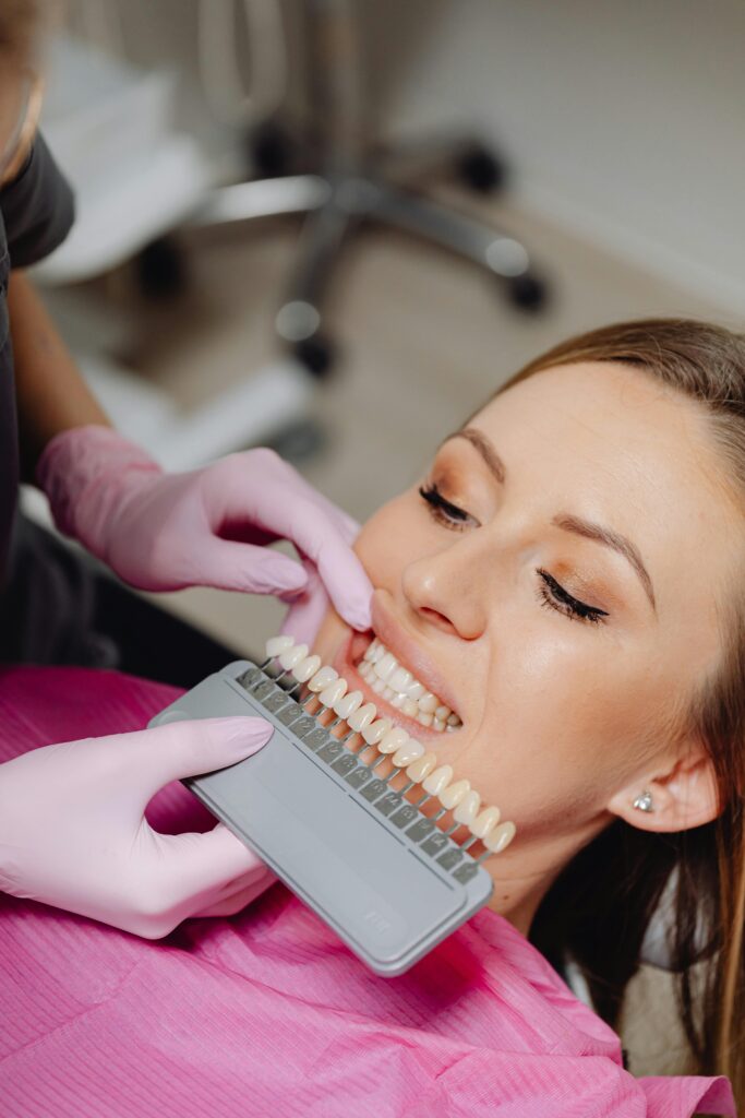 pexels-photo-6627562-6627562 A woman undergoing a dental check-up with a shade guide to match teeth color in a dental clinic.