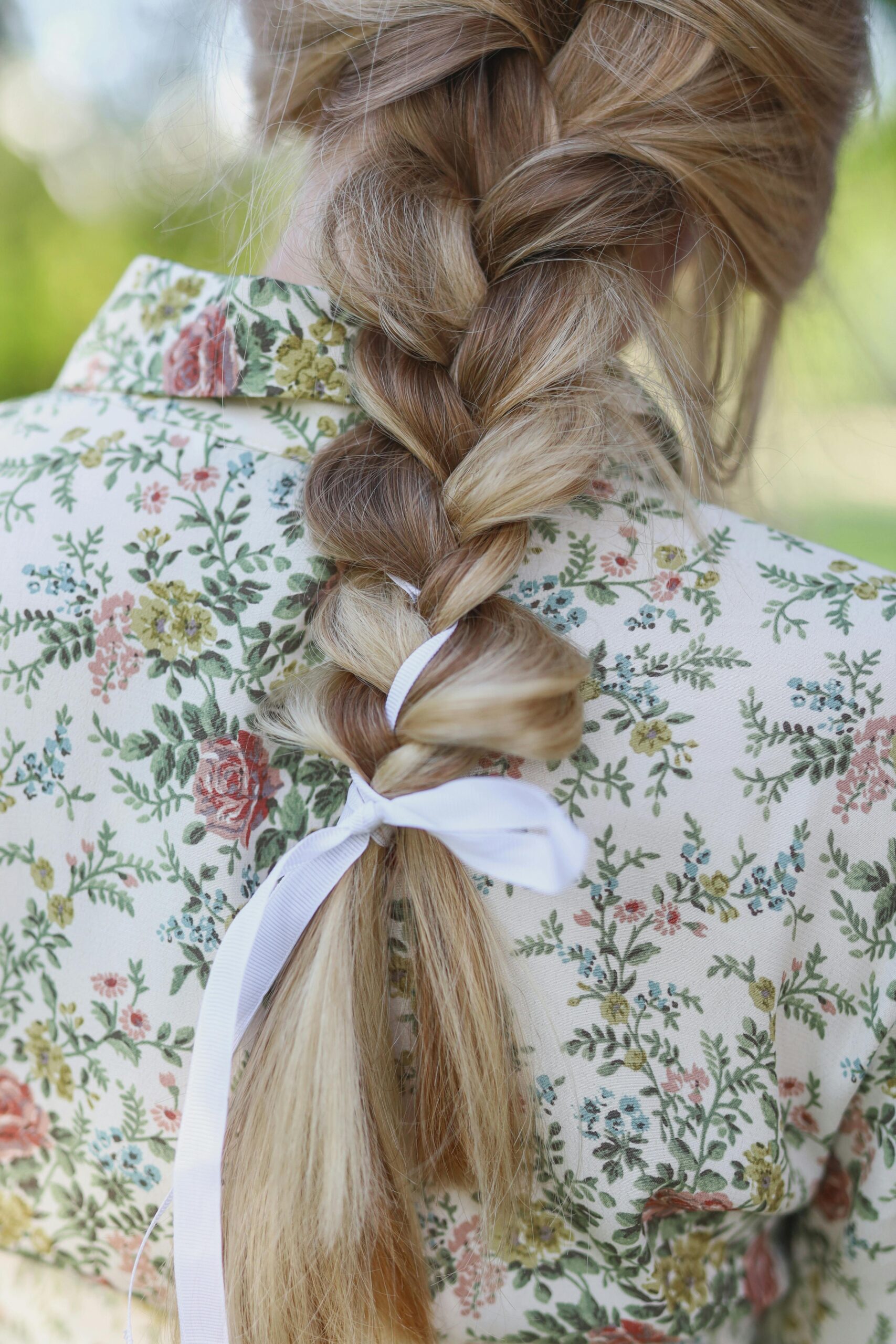 A detailed shot of a braided hairstyle tied with a white ribbon against floral patterned clothing.
