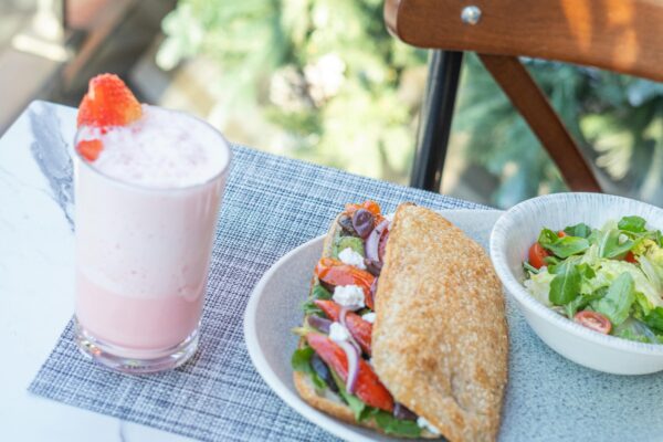 Delicious sandwich, salad, and pink smoothie on a marble table outdoors.