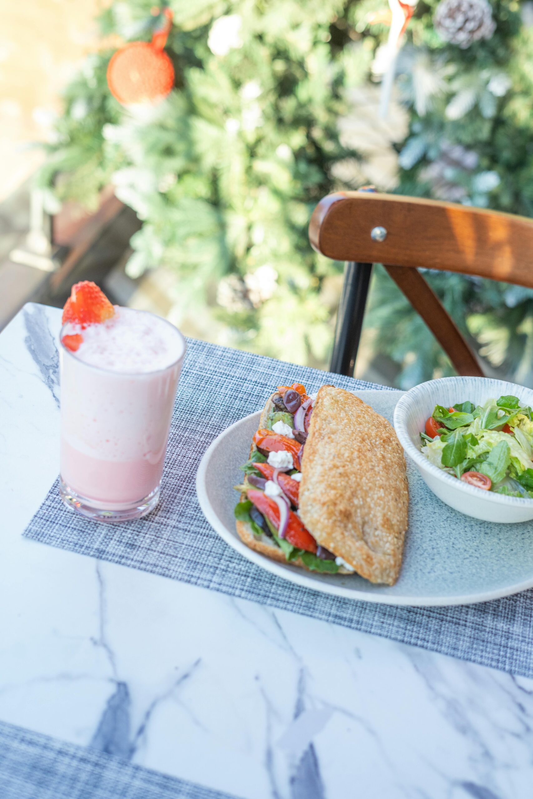 Delicious sandwich, salad, and pink smoothie on a marble table outdoors.