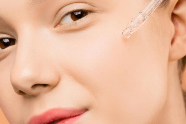 A woman applying serum with a dropper to her face for skincare routine.